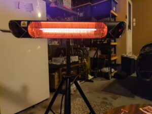 Briza infrared electric patio heater glowing red on a tripod stand in a garage workshop
