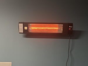 Wall-mounted Dr. Infrared Heater DR-238 glowing on L3, black infrared heater with power cord hanging down