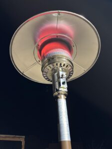 Close-up of the EAST OAK patio heater burner glowing red beneath the round reflector at night.