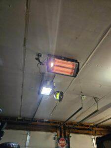 Ceiling-mounted Shinic radiant quartz garage heater with work light on and glowing orange tubes
