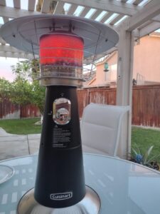Cuisinart COH-514 tabletop patio heater lit on a glass patio table under a pergola, radiant burner glowing red Image 3 (backyard a