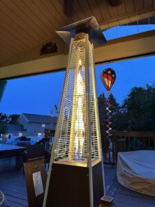 EAST OAK pyramid propane patio heater with glass tube flame glowing on a covered deck at dusk