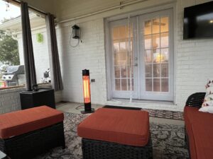 Infrared tower patio heater glowing on a covered outdoor seating area with wicker furniture and glass doors.