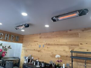 Two Briza infrared heaters mounted to the ceiling in a room with wood-plank walls and recessed lights