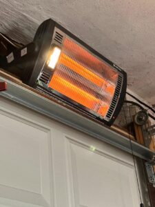 Comfort Zone dual quartz radiant heater installed above a garage door, heating tubes glowing with the work light on.