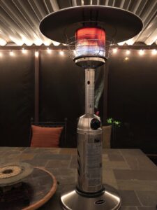 Hiland HLDS032-CG tabletop propane patio heater glowing red under a covered patio with string lights.