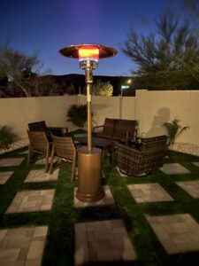 EAST OAK patio heater glowing in a backyard patio seating area with wicker chairs at dusk.