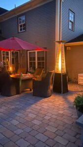 Pamapic pyramid patio heater lit at night next to a patio seating area with table, chairs, and umbrella