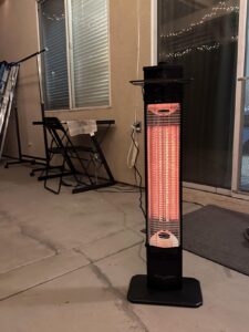 Close-up of the Encyclpo infrared tower heater running at night on a patio near a sliding glass door.