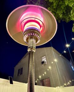 Close-up of Hiland HLDS01-WCGT propane patio heater burner and reflector glowing at night with backyard string lights.