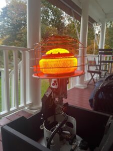 Mr. Heater MH540T radiant tank-top heater glowing bright orange on a covered porch, mounted to a propane tank