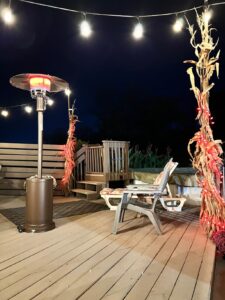 EAST OAK patio heater warming a wooden deck at night with string lights, lounge chair, and seasonal decor.