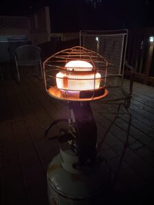 Mr. Heater MH540T tank-top radiant propane heater glowing at night on a deck with patio chairs in the background