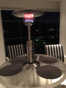 Hiland HLDS032-CG tabletop patio heater lit on a round glass dining table in a screened porch at night.