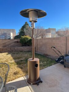 Bronze EAST OAK patio heater on a backyard patio in daylight with round reflector and wheeled base