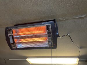 Comfort Zone ceiling-mounted dual quartz heater with glowing elements and pull-chain control mounted above a garage light.