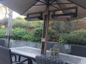 Two ceiling-mounted infrared quartz heaters hanging under a patio umbrella over an outdoor dining table.
