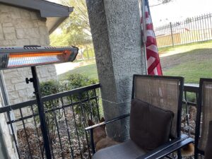 Tripod-mounted Heat Storm infrared heater warming a patio seating area, with a dog resting near the chair