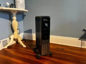 Dreo DR-HSH010 oil-filled radiator heater warming a room beside a wall and wood floor