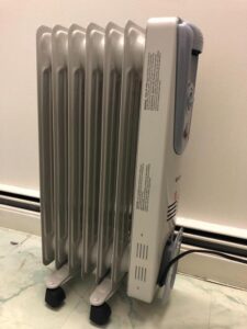 COSTWAY oil-filled radiator heater side view with caster wheels beside a wall baseboard