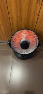 Kismile oscillating parabolic space heater glowing on a tile floor in front of a wooden cabinet