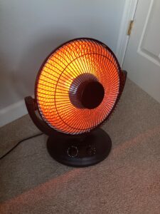 Kismile oscillating parabolic heater glowing orange on carpet near a wall and door